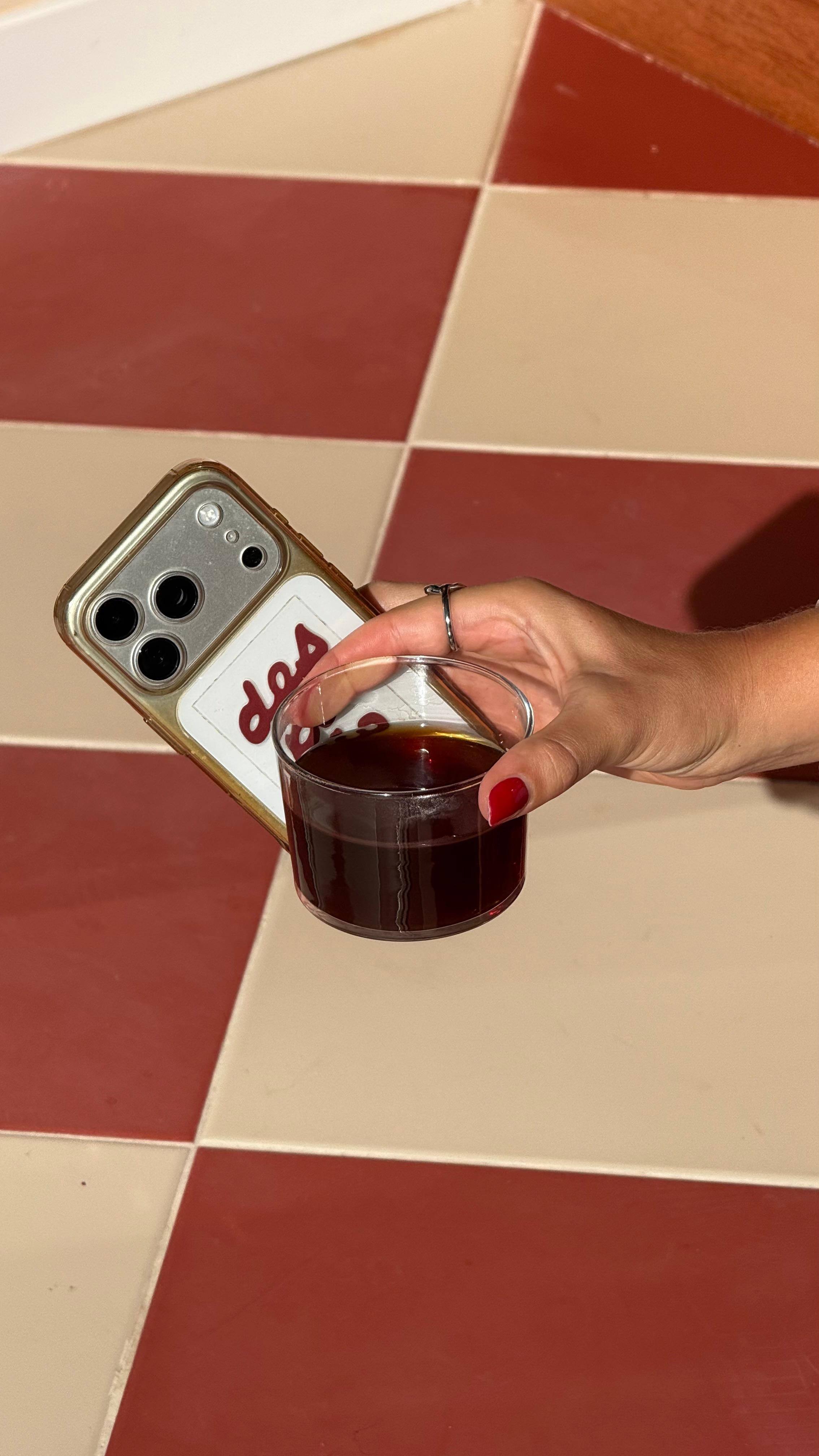 Una mano sostiene un café en vaso de cristal sobre el suelo de baldosas