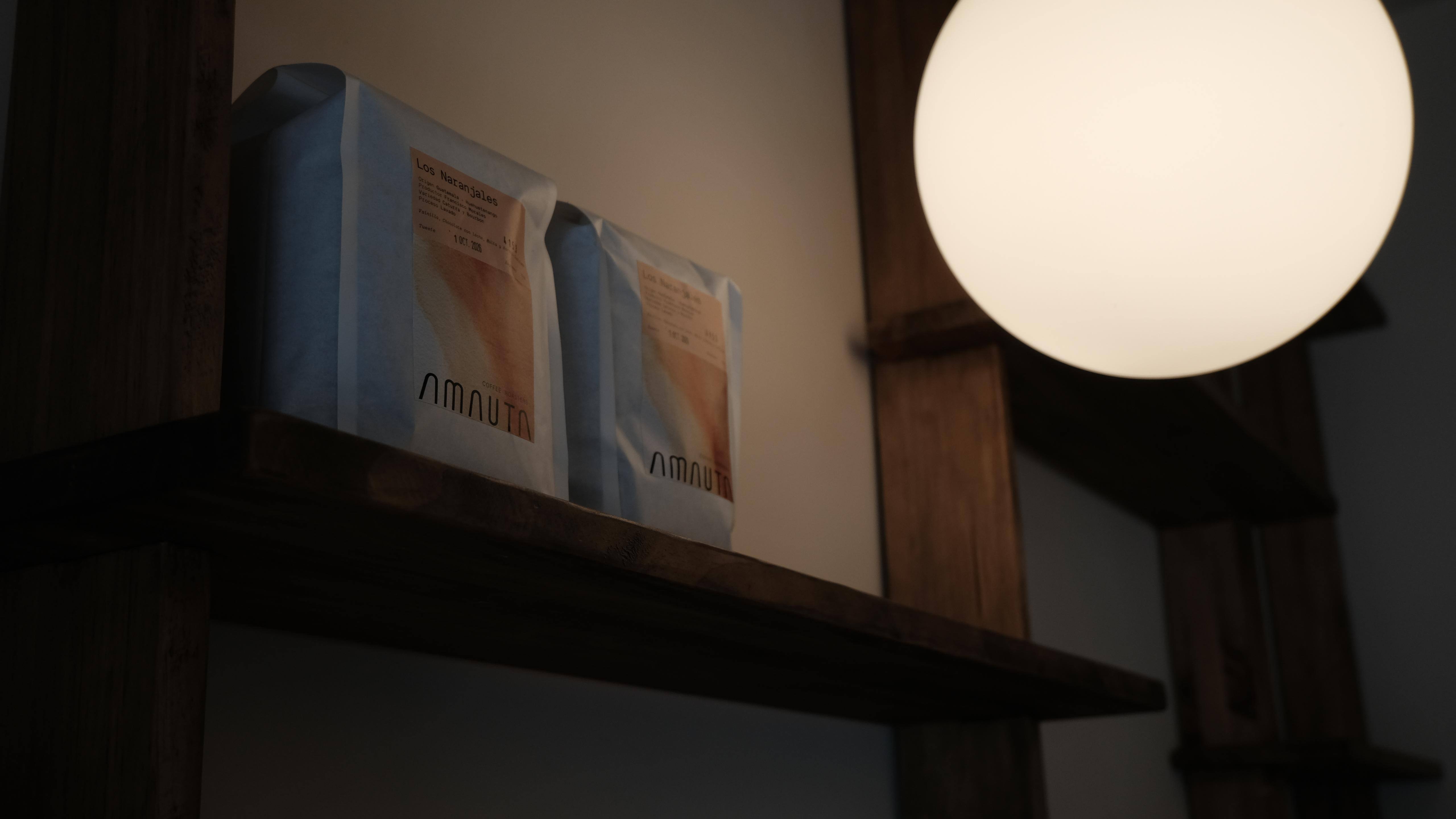 Bolsas de café sobre una estantería de madera junto a una lámpara redonda